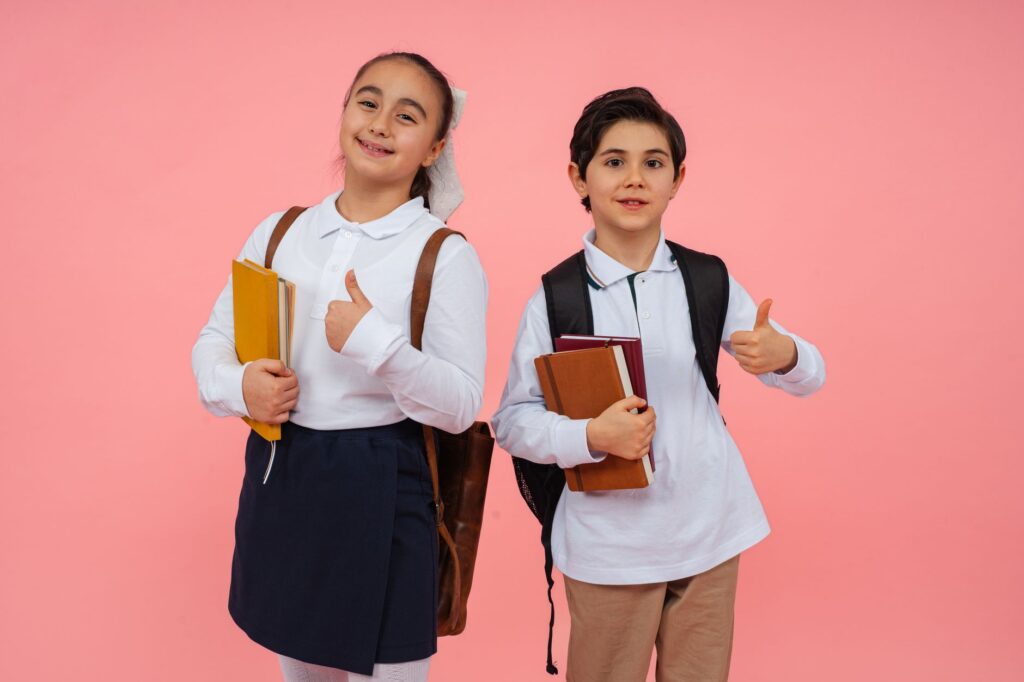 Two children in school uniform with backpacks walking to school in September