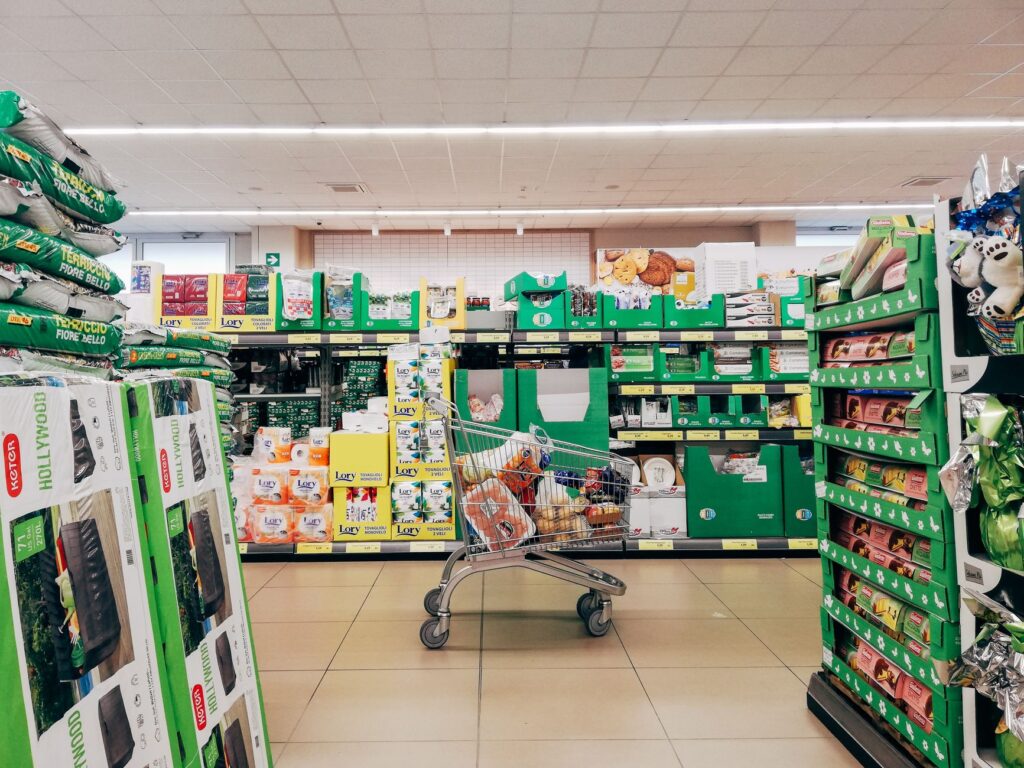 A shopping trolley in a UK supermarket aisle stacked with grocery items, illustrating a 2026 supermarket price comparison