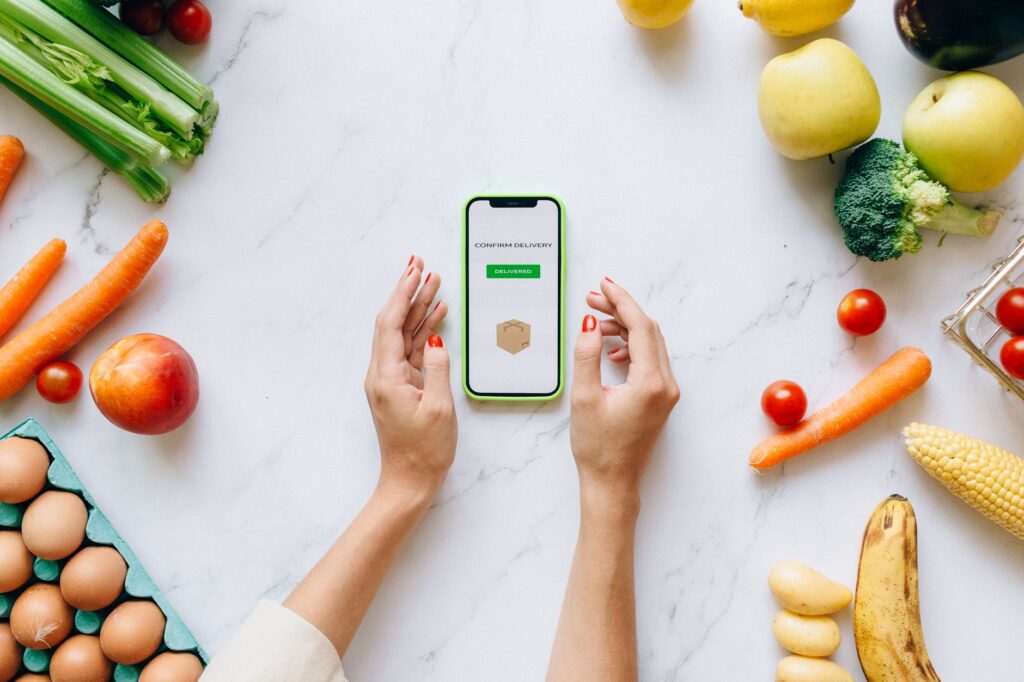 A smartphone showing a food waste app next to a supermarket basket of yellow sticker reduced food
