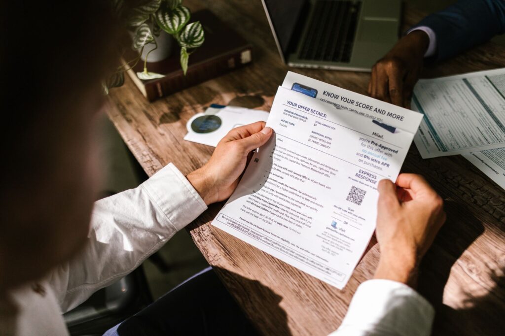 An investor at a desk reviewing printed share dividend statements alongside a calculator and laptop.