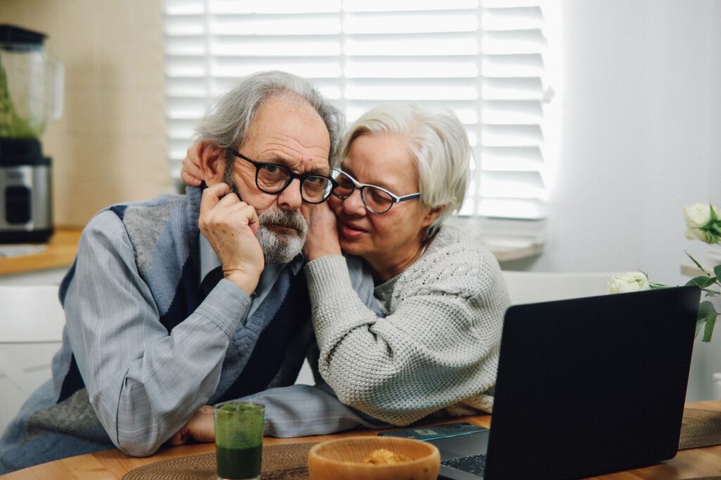An older couple sitting at a kitchen table going through mortgage paperwork together with a calculator and a laptop.