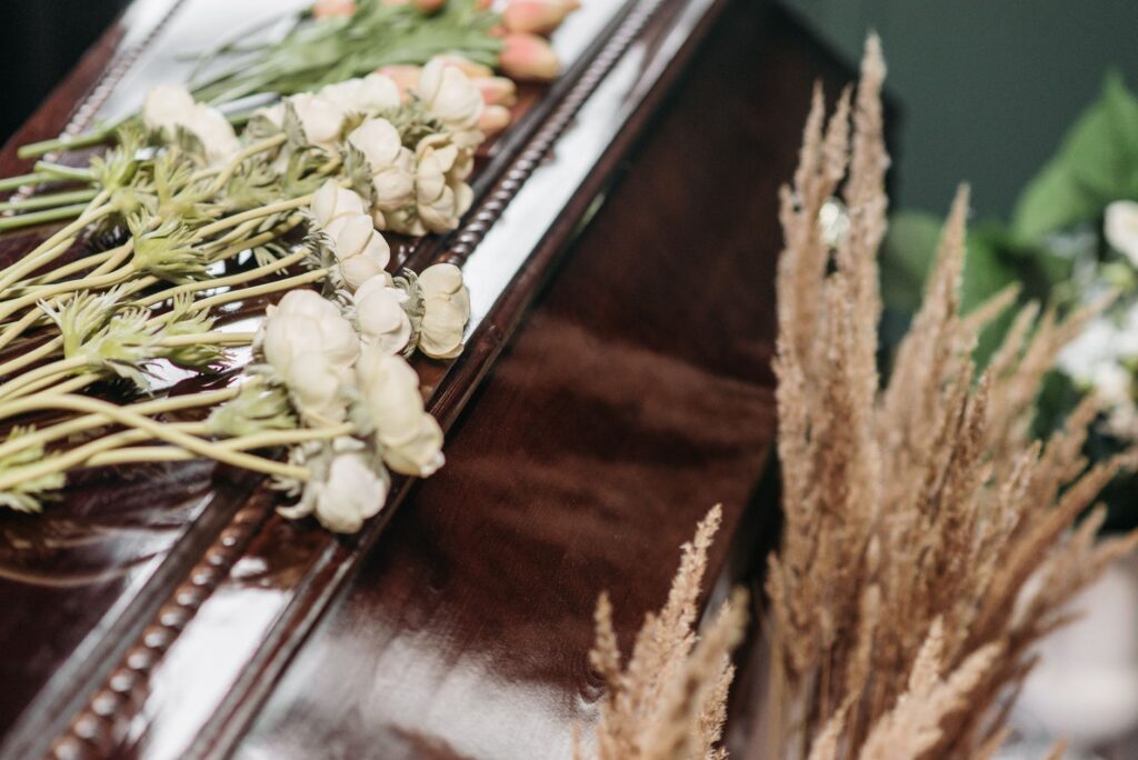 A spray of white flowers resting on a plain wooden coffin in a quiet chapel.