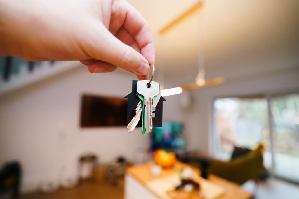 A hand holding a set of house keys in the doorway of a rented home.
