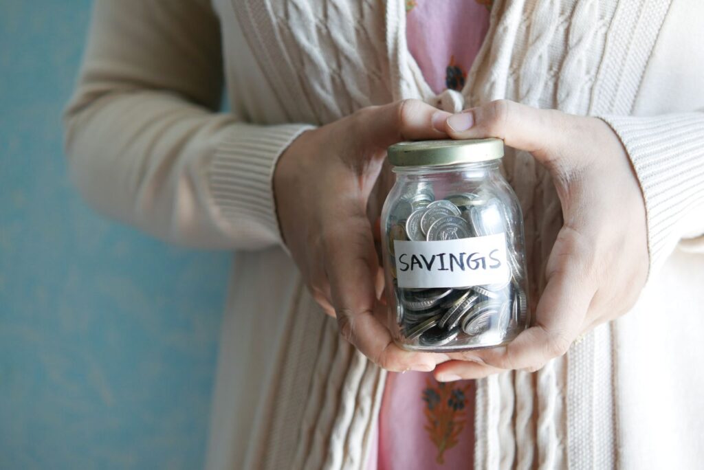 A pair of hands holding a glass savings jar filled with coins.