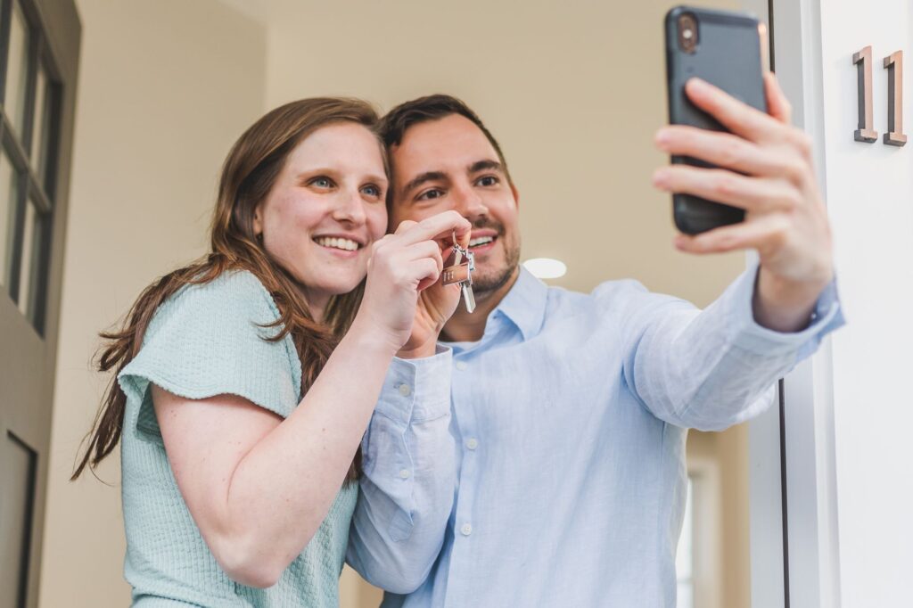 A young couple standing in the doorway of a new-build flat holding a set of keys and a folder of paperwork.
