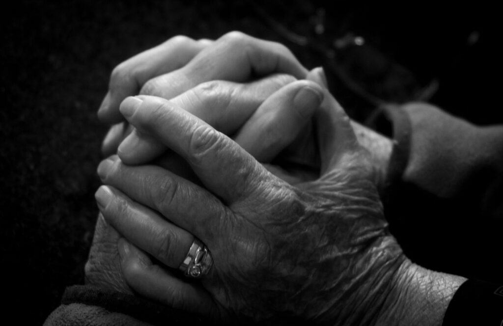 A black and white close-up of a younger person's hand holding an older person's hand.