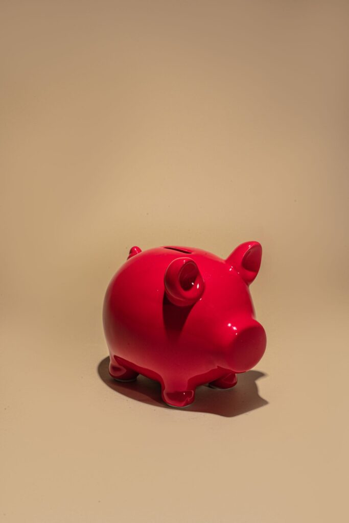 A red ceramic piggy bank standing on a plain beige background.